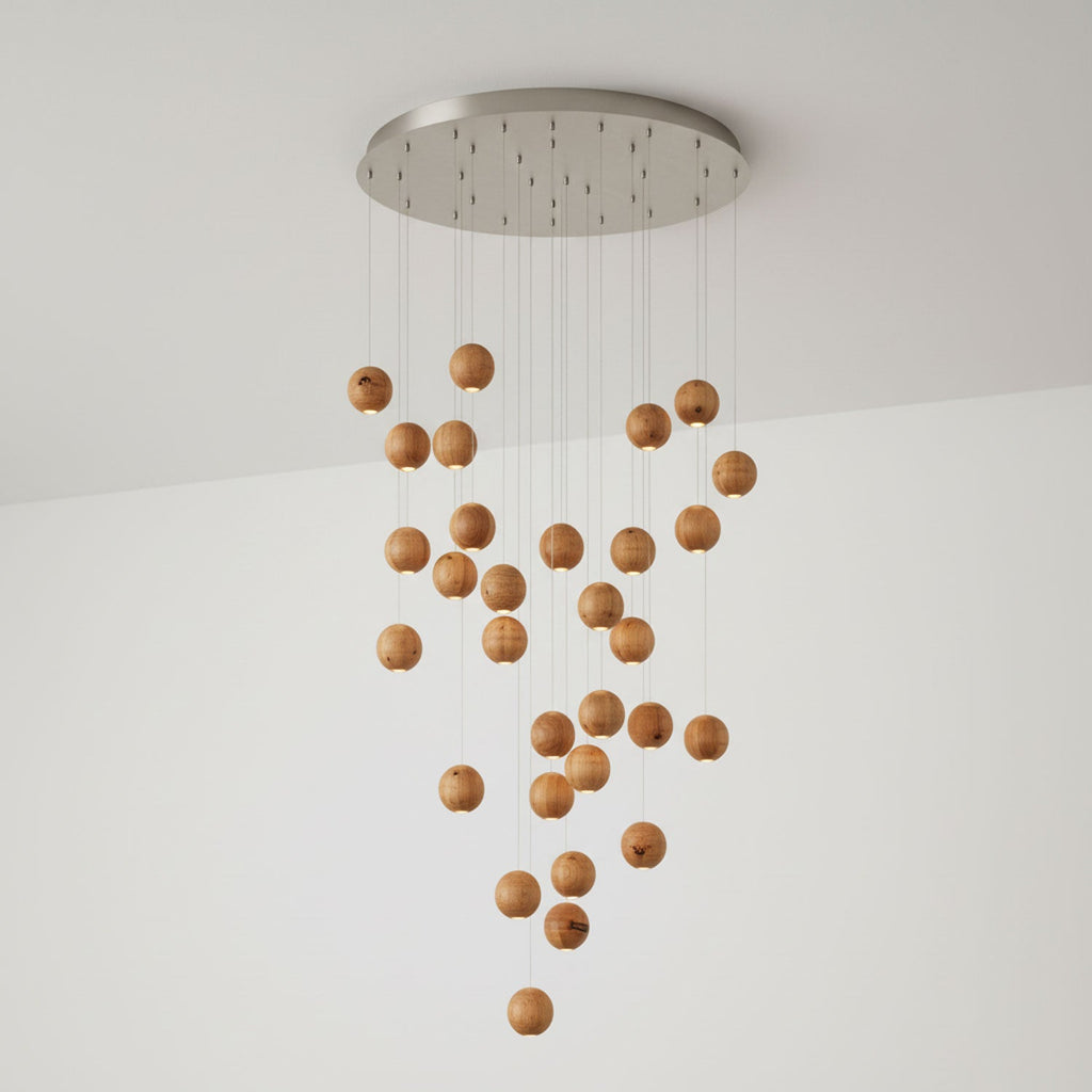 A Clérachic pendant with many wood spheres cascading from a round brushed-metal ceiling plate, against a white wall.