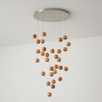 A Clérachic pendant with many wood spheres cascading from a round brushed-metal ceiling plate, against a white wall.