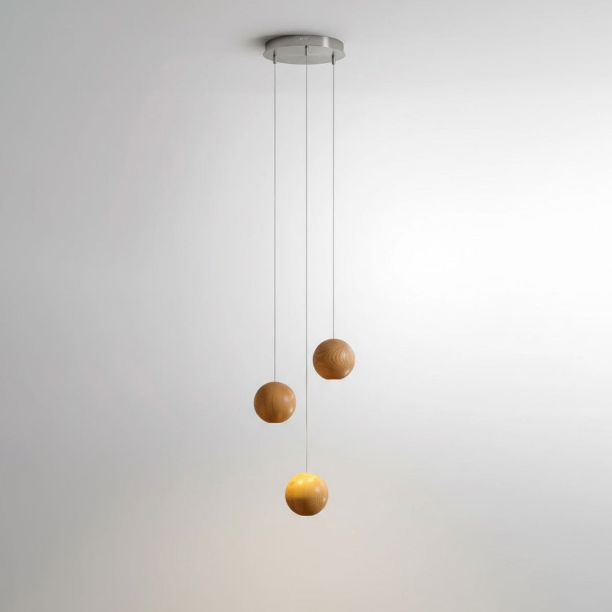 A three-sphere Clérachic wood pendant on a small round ceiling plate, one sphere glowing warm below two unlit spheres.