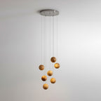 A Clérachic wood-sphere pendant on a round ceiling plate, with a few spheres lit warmly, against a soft grey wall.