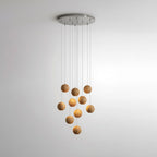 A Clérachic wood pendant on a round metal ceiling plate, its spheres hung at staggered heights against a pale wall.