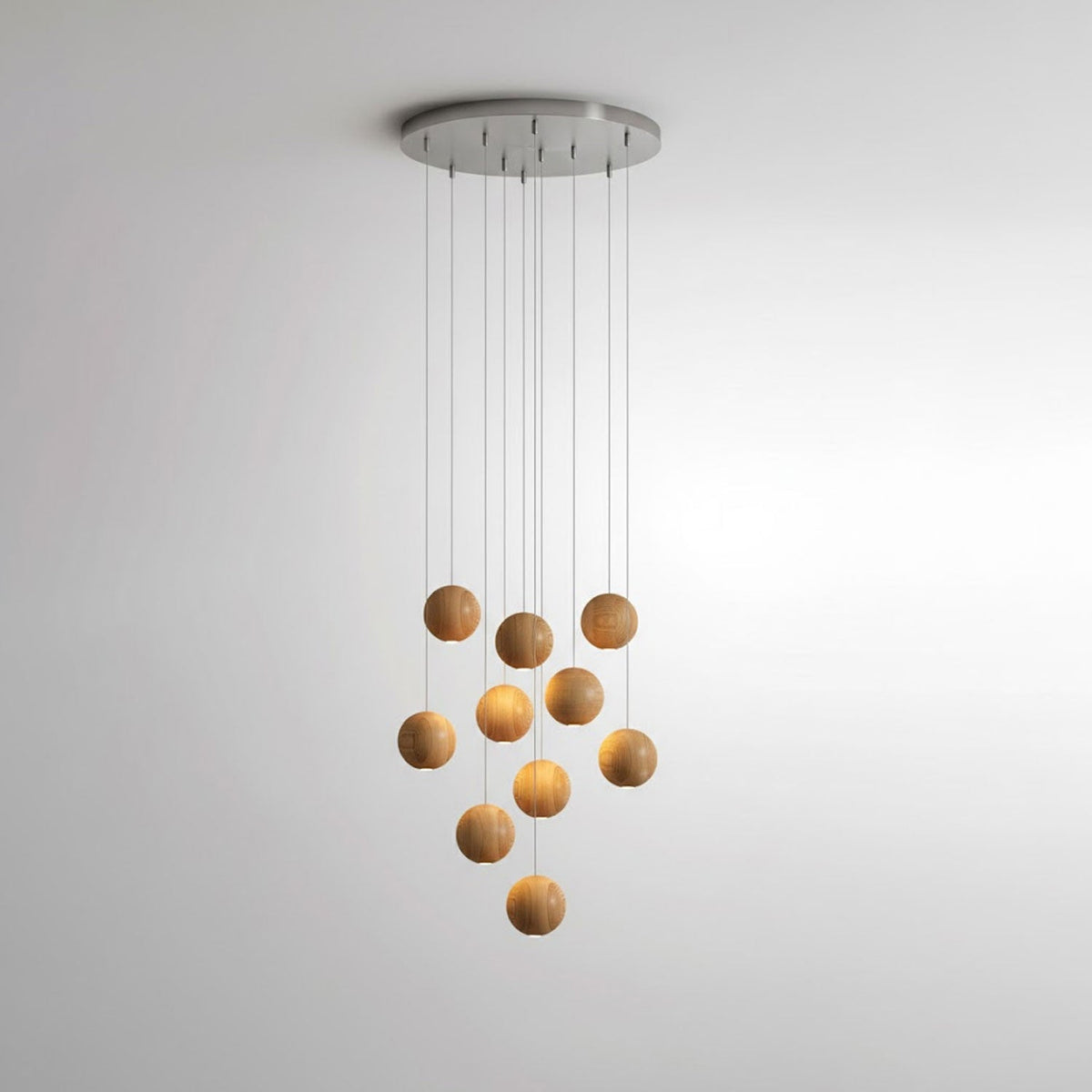 A Clérachic wood pendant on a round metal ceiling plate, its spheres hung at staggered heights against a pale wall.