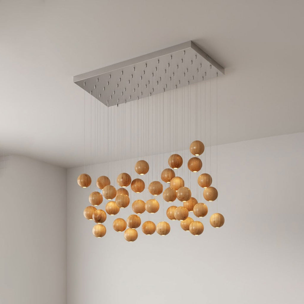 A dense Clérachic cluster of wood spheres, lit warmly, hung below a long rectangular brushed-metal ceiling plate in a corner room.