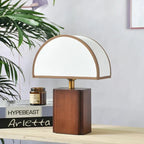 Clérachic table lamp in the Brown & White option, close enough to show the brown binding around the shade's curved edge, on a wooden shelf beside a stack of books and an amber candle jar.