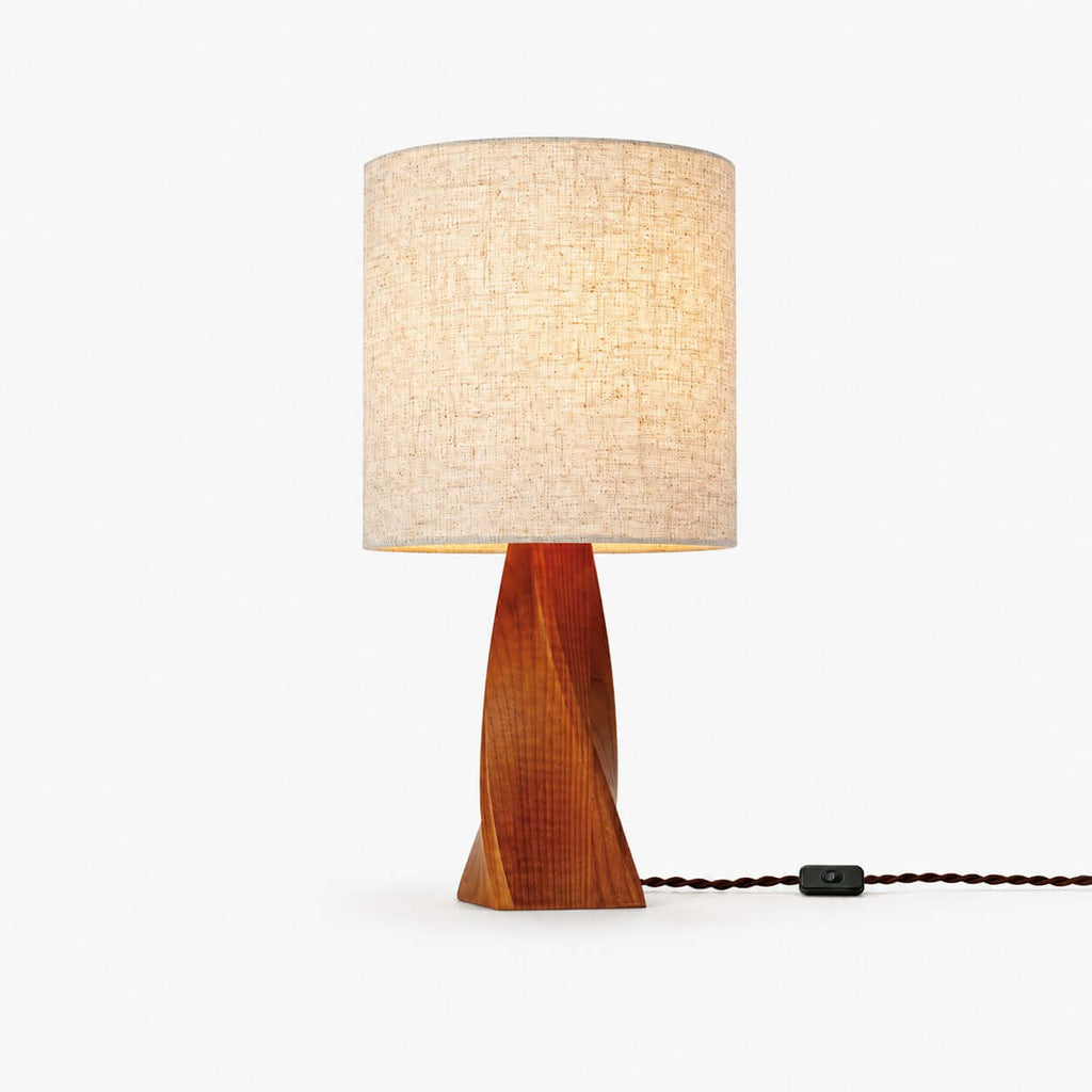 A twisted wooden base in warm brown wood carries a beige linen drum shade, with a braided cord and in-line switch, on white for this Clérachic table lamp.