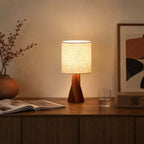 This Clérachic table lamp lights a dark wooden sideboard with an open book, a glass of water, a terracotta pot and a rust-and-black print.