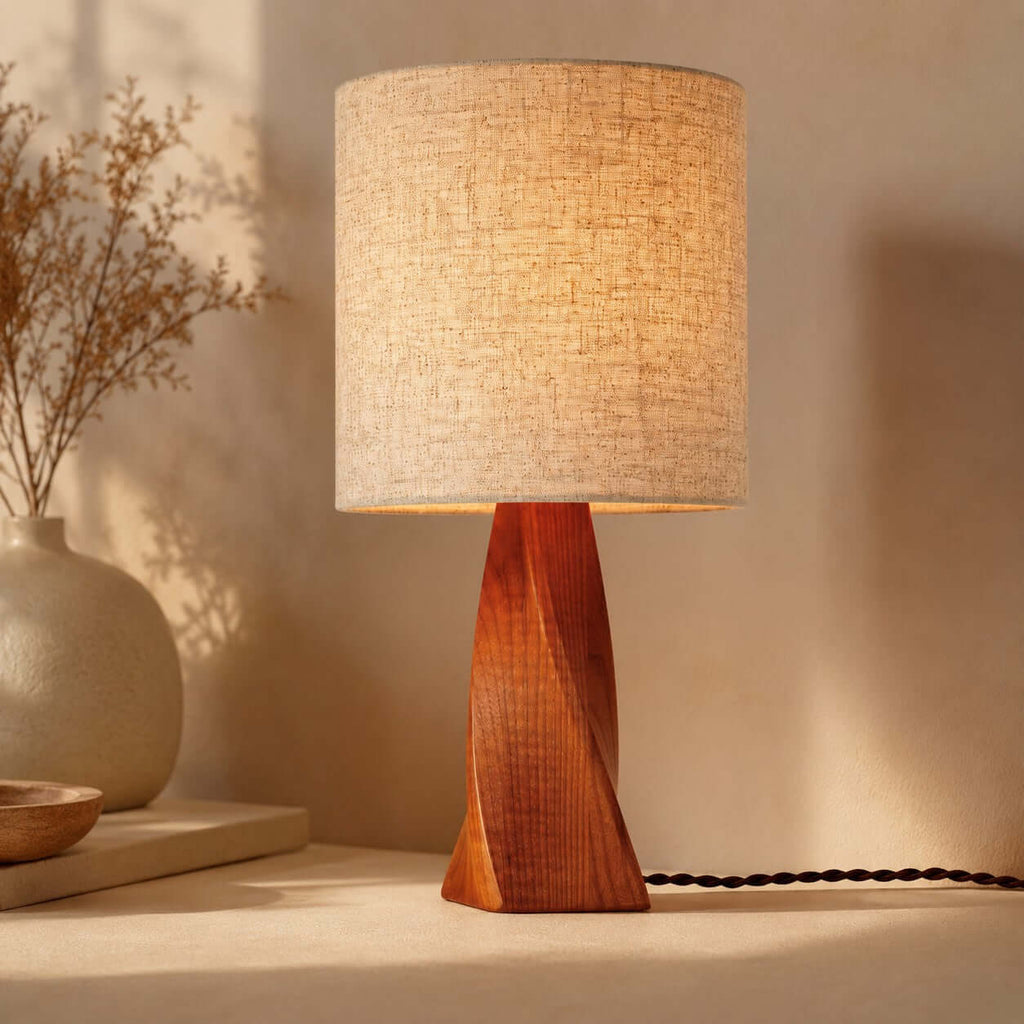 Close view of the twisted grain of the wooden base and the textured beige linen shade of this Clérachic table lamp, with a braided black cord.