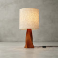 This Clérachic table lamp stands unlit on a pale concrete floor against a grey wall, with its braided black cord and switch trailing to one side.