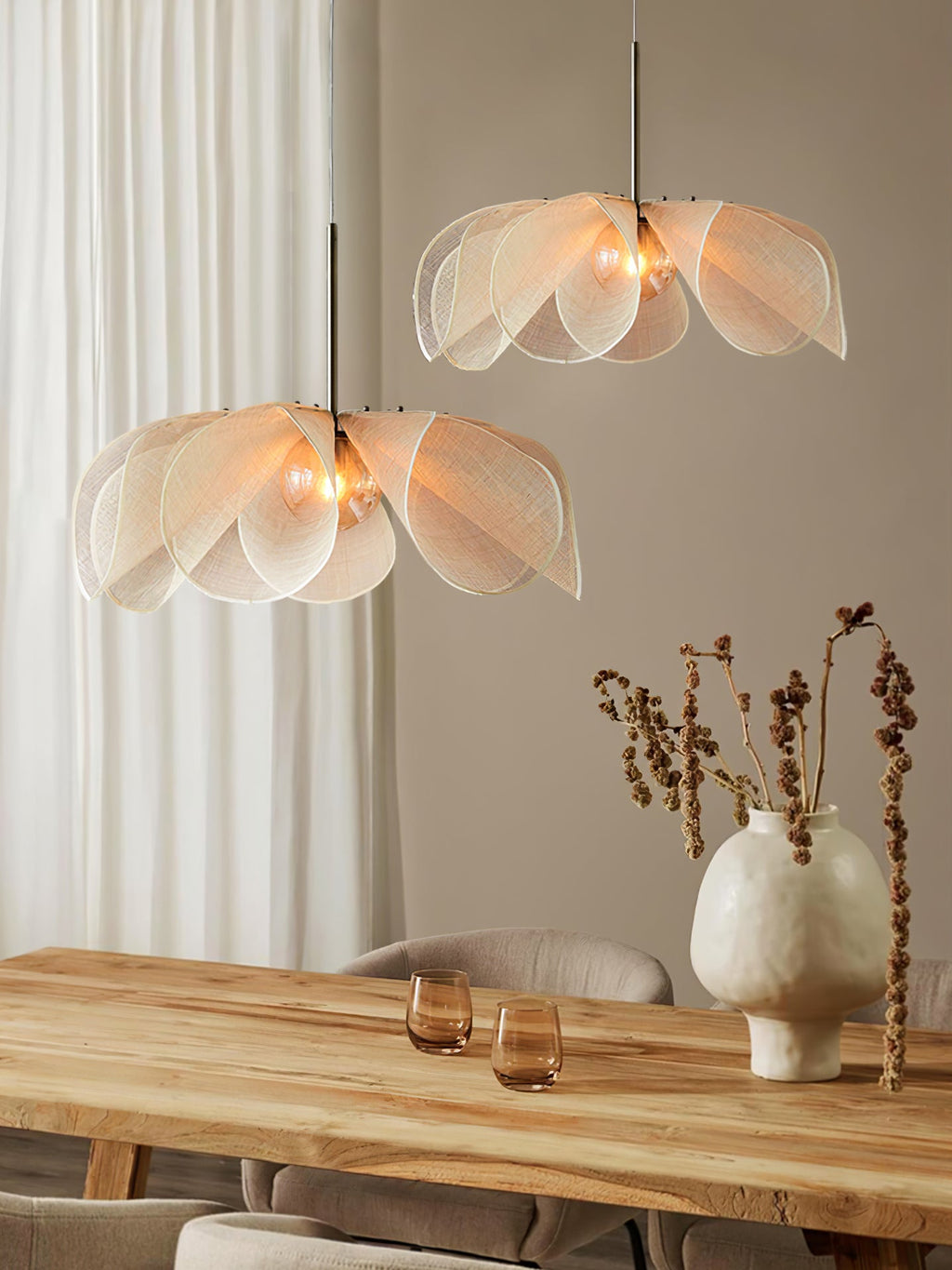 Two Clérachic pendants with layered fibre petals hang at different heights above a pale wood dining table and a ceramic vase.
