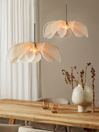 Two Clérachic pendants with layered fibre petals hang at different heights above a pale wood dining table and a ceramic vase.