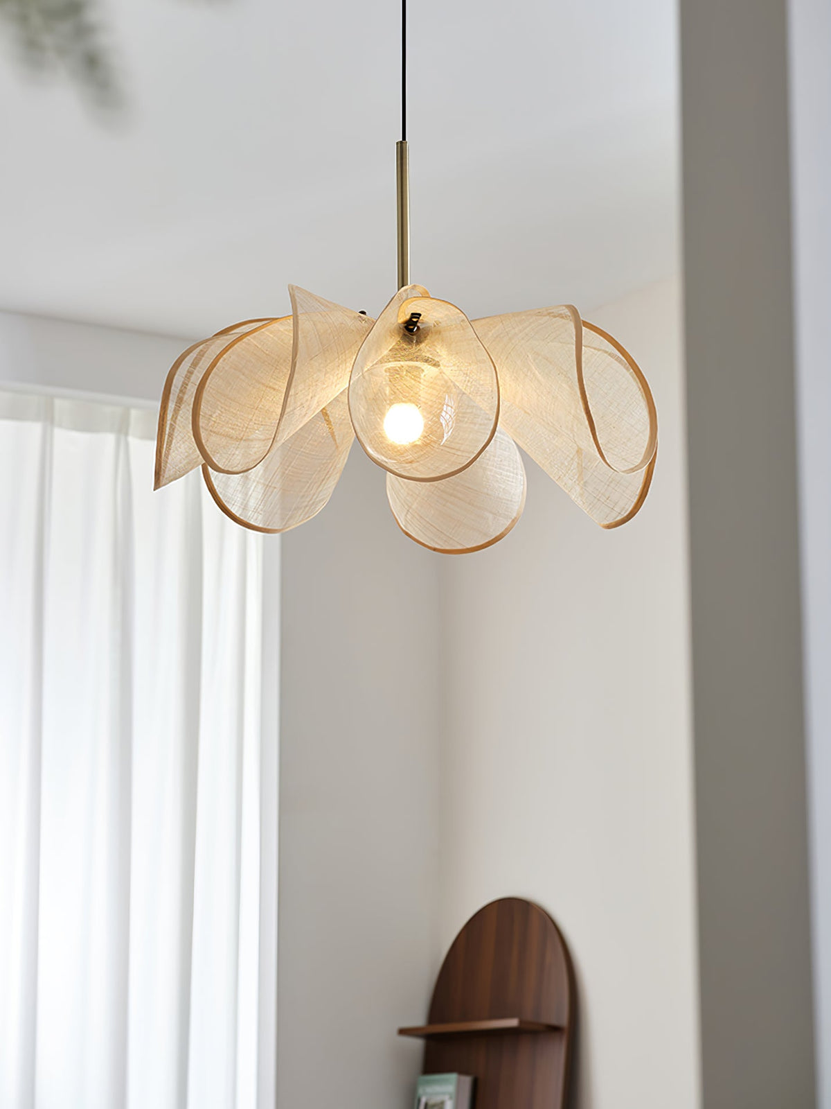 Lit bloom shade with a gold-toned stem hung near a sheer-curtained window, a Clérachic pendant seen from below.