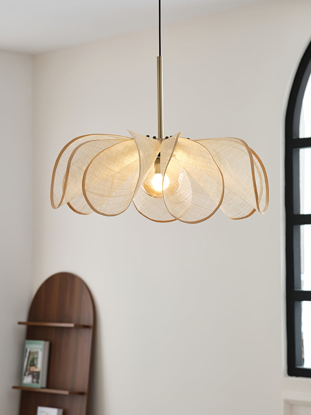Wide, flat view of this Clérachic pendant's overlapping woven petals, lit, with an arched window and walnut shelf behind.