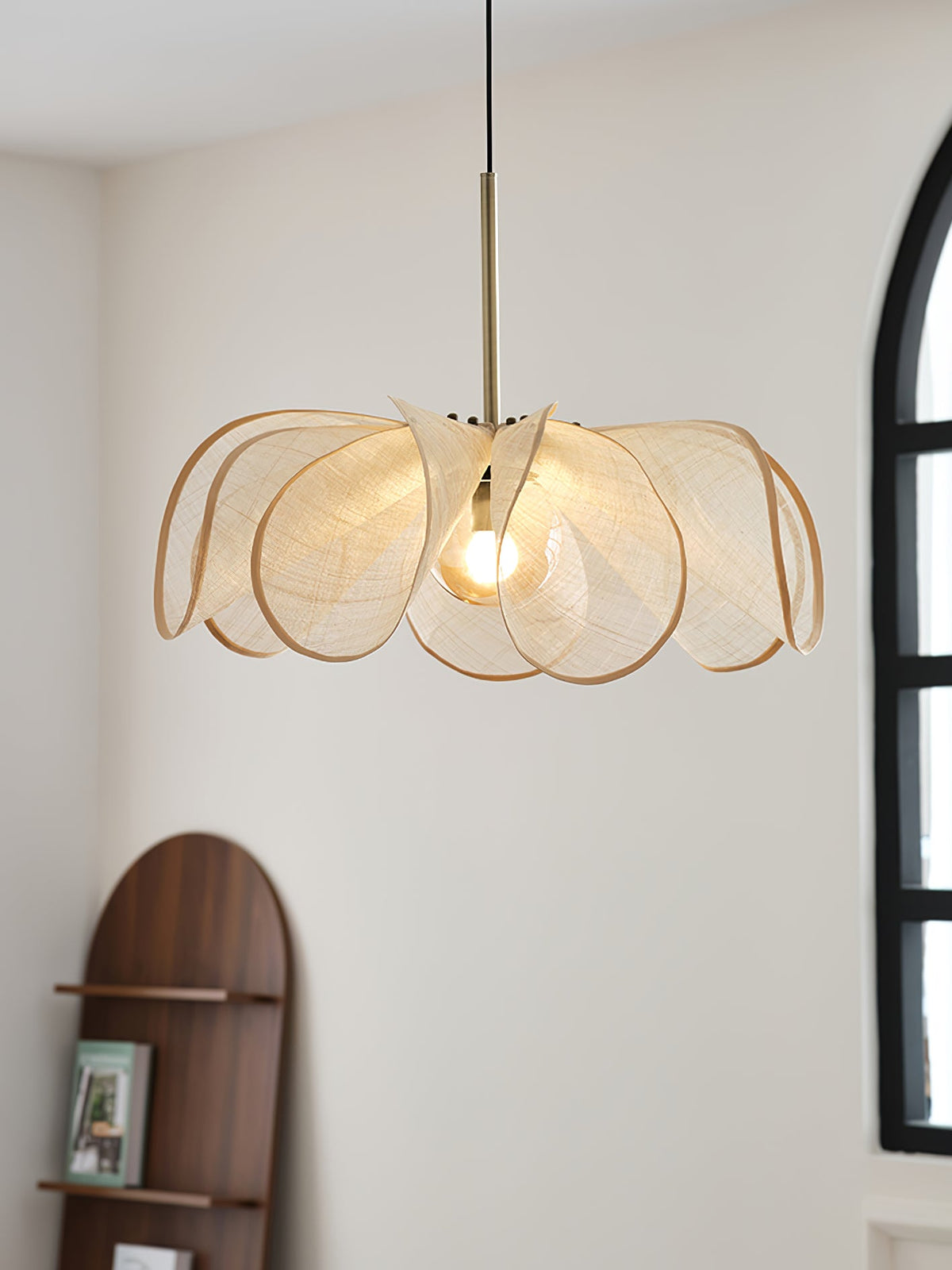 Wide, flat view of this Clérachic pendant's overlapping woven petals, lit, with an arched window and walnut shelf behind.