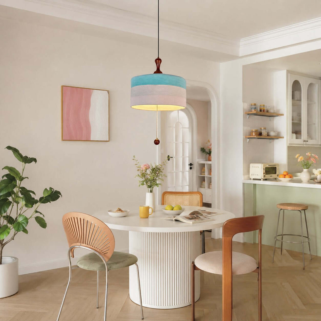 This Clérachic pendant in blue and white hangs in a bright dining nook with a white pedestal table and a pale green kitchen beyond.