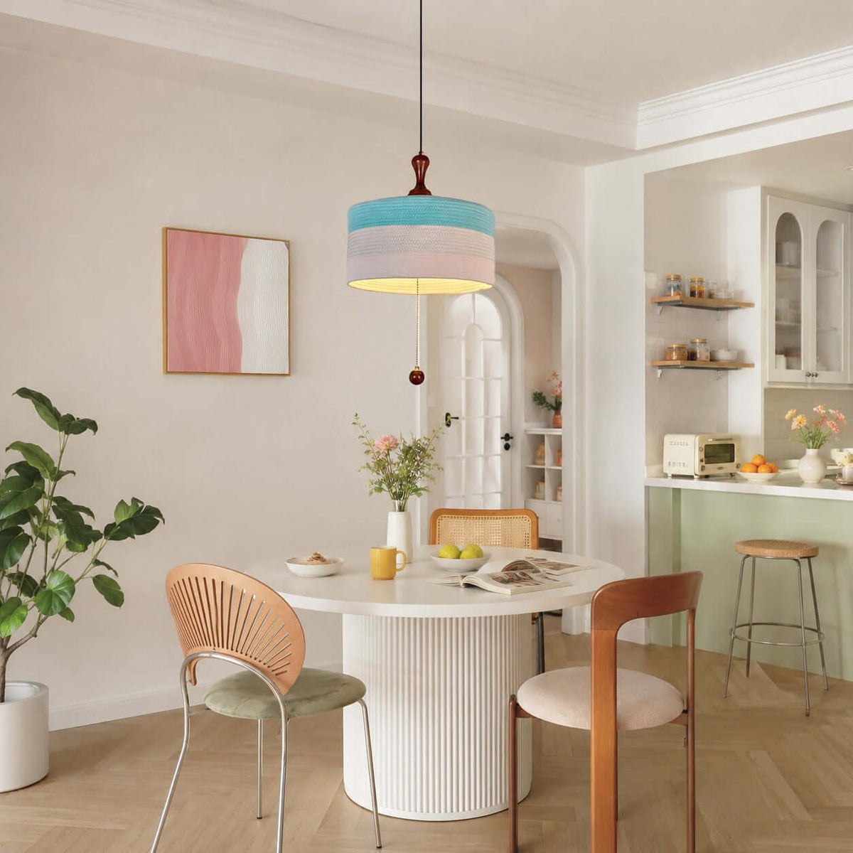 This Clérachic pendant in blue and white hangs in a bright dining nook with a white pedestal table and a pale green kitchen beyond.