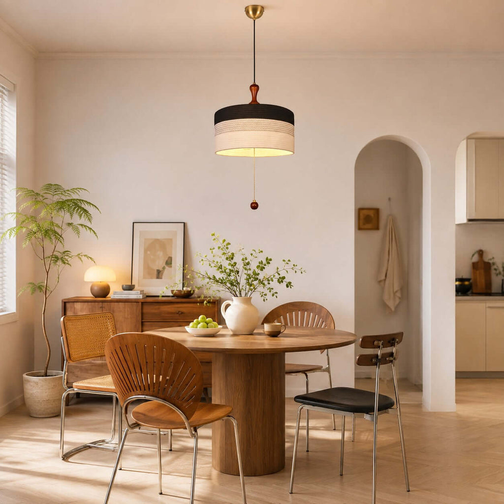 A black and white Clérachic drum pendant hangs low over a small round table in a warm, peach-toned room with an archway.