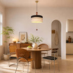 A black and white Clérachic drum pendant hangs low over a small round table in a warm, peach-toned room with an archway.