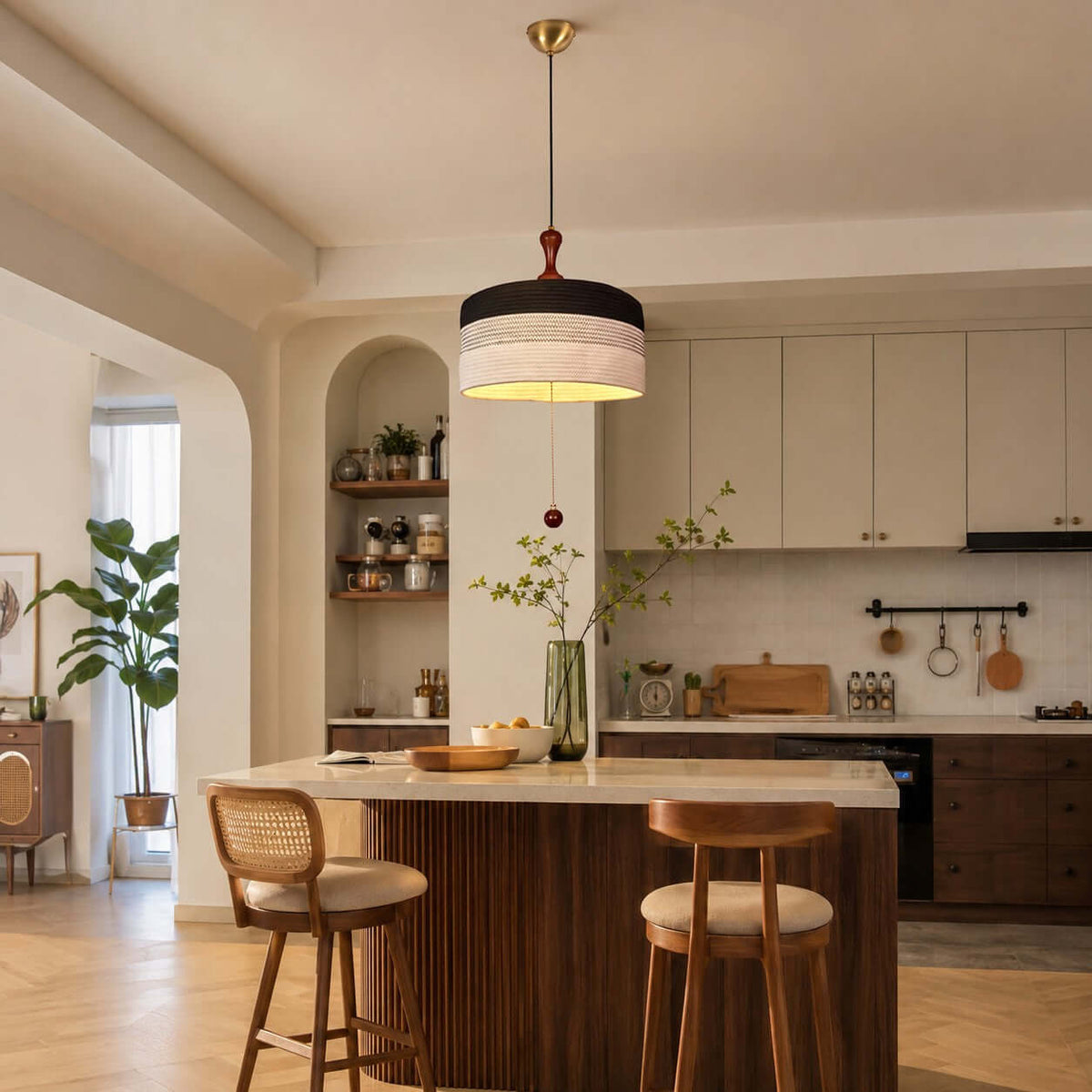 Above a kitchen island with two cane-backed stools, this Clérachic pendant shows a black and white woven drum shade.