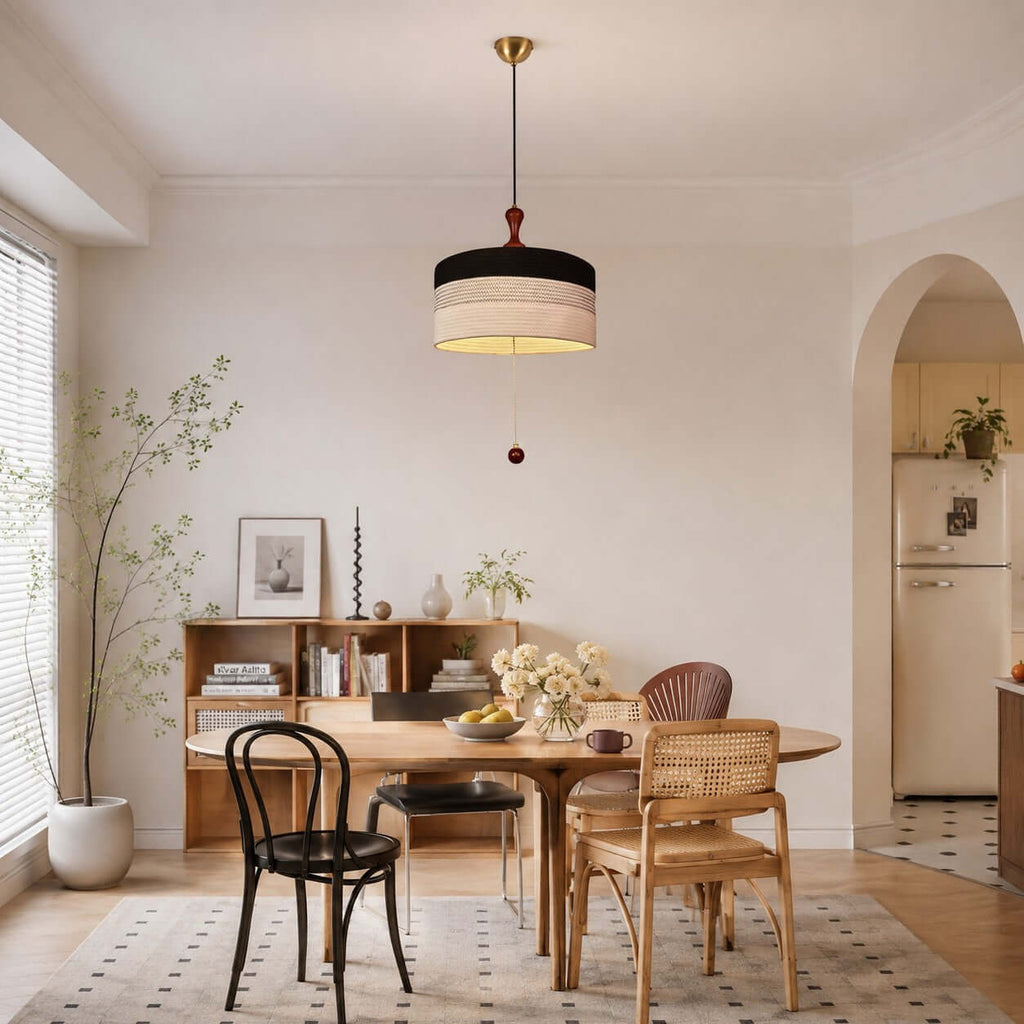 This Clérachic pendant with a black and white fabric drum hangs in a light dining area with a round table and bentwood chair.