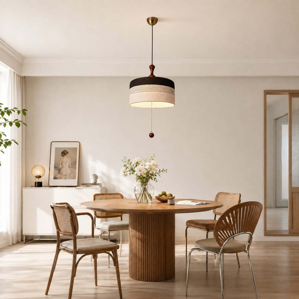 A black and white Clérachic drum pendant lights a round ribbed table with flowers, in a room with a tall mirror.