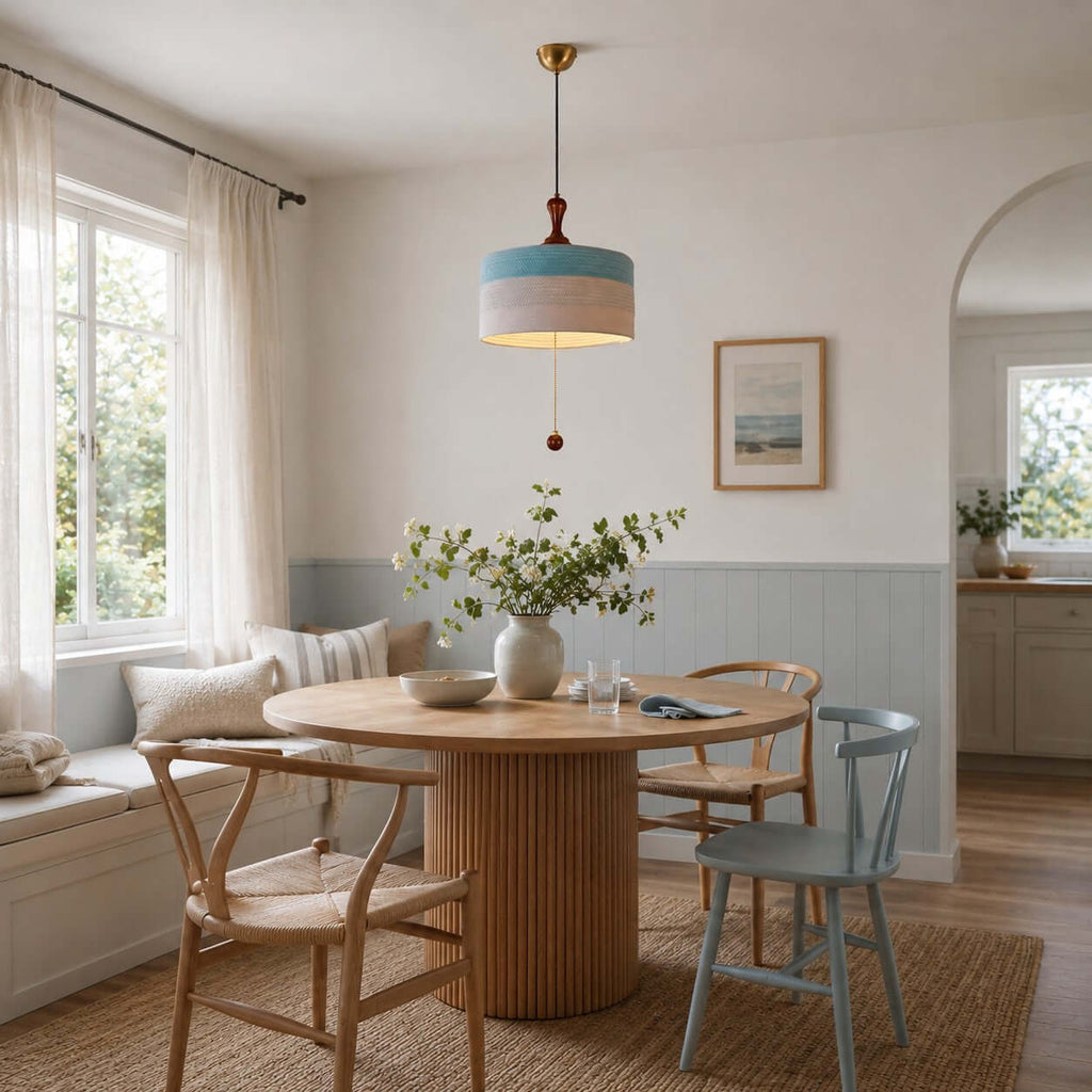 This Clérachic pendant in blue and white hangs in a bright breakfast corner with a round oak table and a window seat.