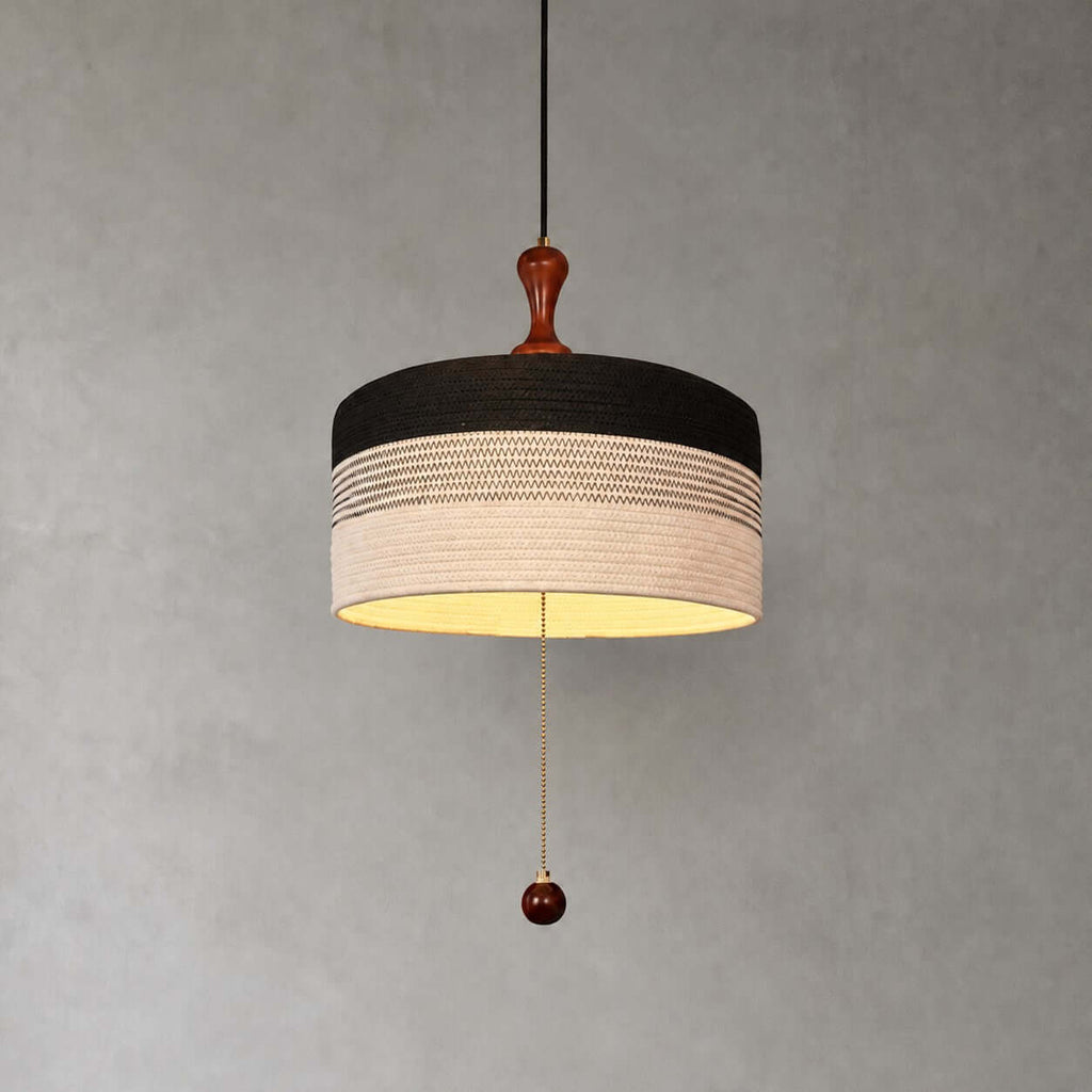 Black and white woven drum shade with a patterned band, wooden finial and pull chain on this Clérachic pendant, on grey.