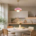 Over a round white table with a lemon bowl, this Clérachic pendant shows a pink woven shade and a warm-lit glass globe.