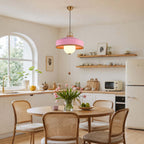 A pink-shaded Clérachic pendant with a wooden pull bead hangs in a kitchen with an arched window and cane-backed chairs.