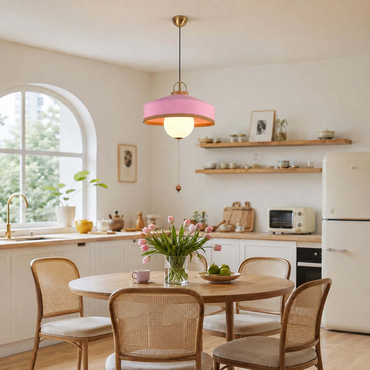 A pink-shaded Clérachic pendant with a wooden pull bead hangs in a kitchen with an arched window and cane-backed chairs.