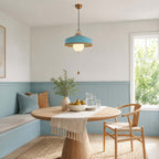 A blue Clérachic pendant hangs over a round table with a fringed runner, in a nook with pale blue panelling.