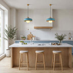 Two blue-shaded Clérachic pendants with pull chains hang above a pale wood kitchen island with three stools.