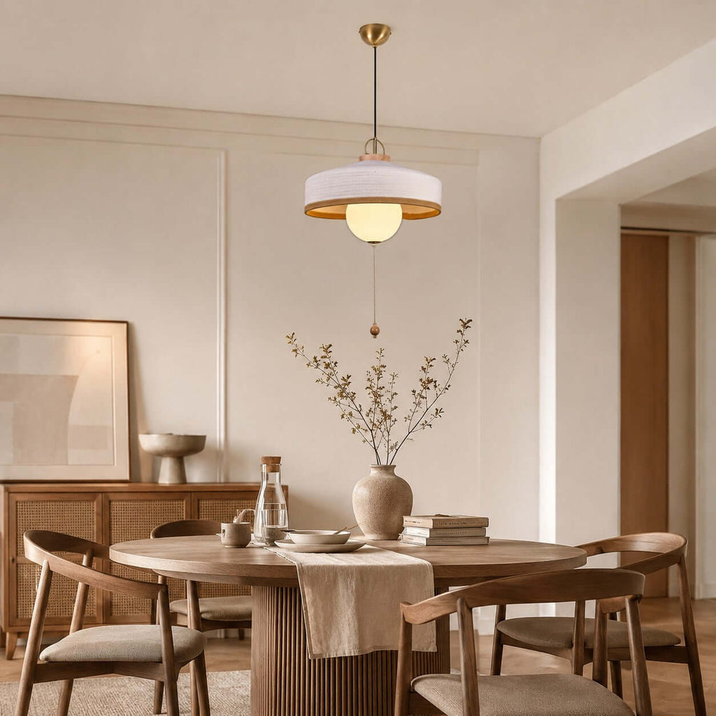 A white woven shade with a gold-toned inner rim on this Clérachic pendant, hung above a round table with a ribbed base.