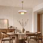 A white woven shade with a gold-toned inner rim on this Clérachic pendant, hung above a round table with a ribbed base.