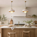 Two white-shaded Clérachic pendants with glass globes hang over a kitchen island with a brass tap and straw stools.