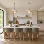 A pair of white Clérachic pendants hangs above a long marble island with four grey-green upholstered stools.