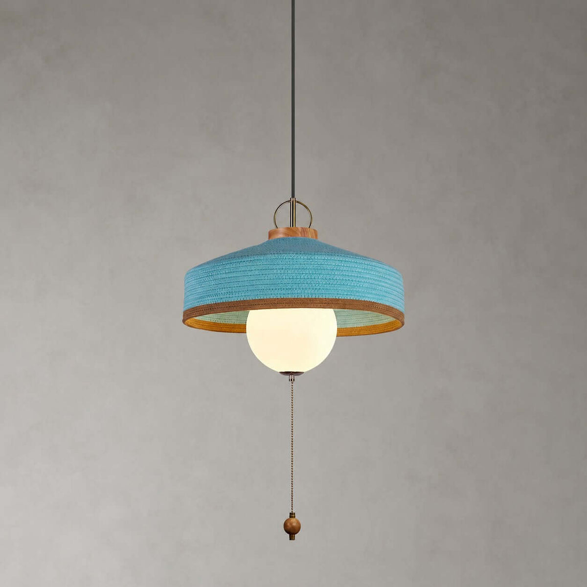 Blue woven shade with a copper-toned inner rim, white glass globe and wooden pull bead on this Clérachic pendant, on grey.