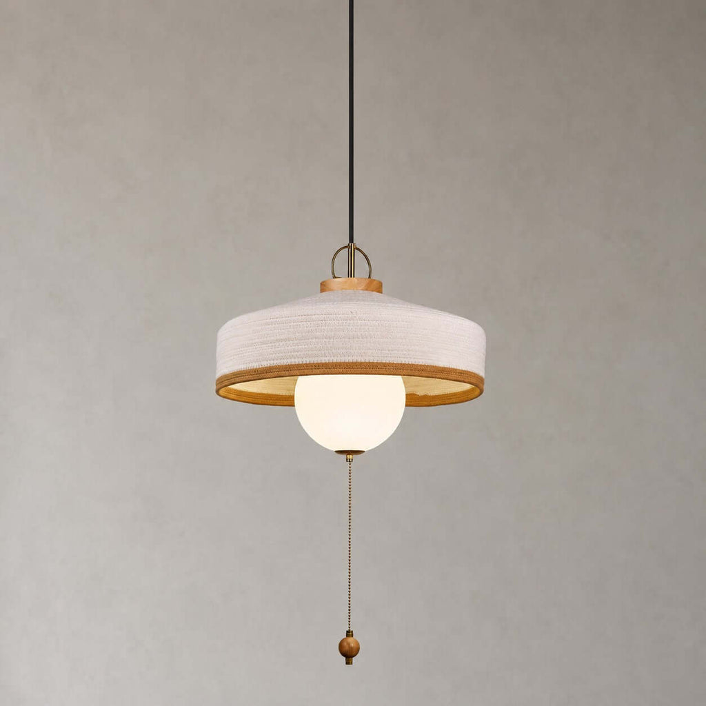 A white woven shade over a glass globe, with a beaded pull chain and wooden bead, on this Clérachic pendant on grey.