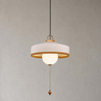 A white woven shade over a glass globe, with a beaded pull chain and wooden bead, on this Clérachic pendant on grey.
