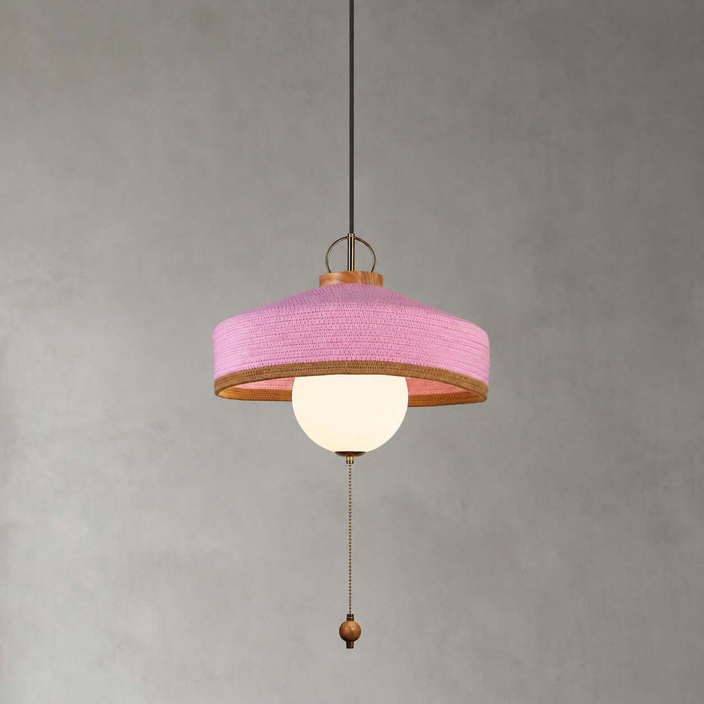 This Clérachic pendant in pink has a woven shade, a white glass globe and a long pull chain, shown on a grey backdrop.