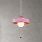 This Clérachic pendant in pink has a woven shade, a white glass globe and a long pull chain, shown on a grey backdrop.
