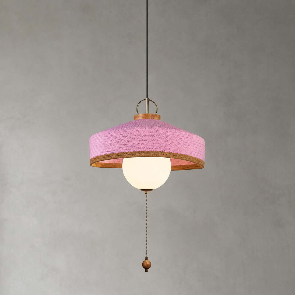 This Clérachic pendant in pink has a woven shade, a white glass globe and a long pull chain, shown on a grey backdrop.