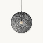A black woven spherical Clérachic pendant light with a bulb glowing inside, hung on a black cord against a white backdrop.