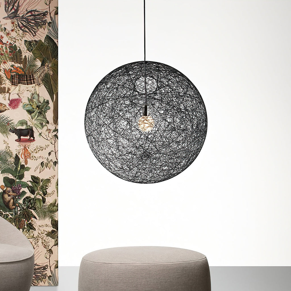 A black woven spherical Clérachic pendant light beside a panel of botanical wallpaper, above a grey round pouffe.