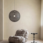 A black woven Clérachic pendant light hung in a calm beige room, above a knotted rope armchair and a chequered side table.