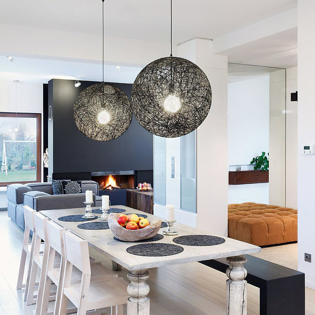 Two black woven spherical Clérachic pendant lights of different sizes above a white dining table, with a fire behind.