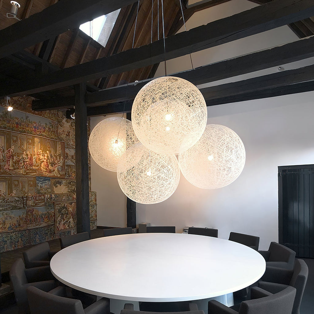 A cluster of off-white woven Clérachic pendant lights lit above a round white table, under dark roof beams.