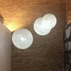 Three off-white woven Clérachic pendant lights of different sizes lit against a warm brick wall.