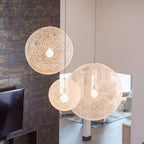 Three off-white woven Clérachic pendant lights glowing at different heights in a living space with a dark tiled wall.