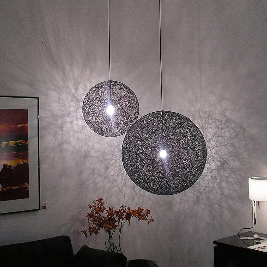 Two black woven Clérachic pendant lights of different sizes lit, throwing a lace-like shadow pattern across a grey wall.