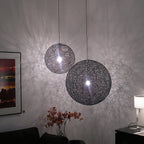 Two black woven Clérachic pendant lights of different sizes lit, throwing a lace-like shadow pattern across a grey wall.